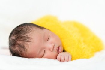 newborn baby sleeping in yellow fur blanket on a bed 