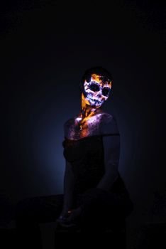 Girl’s Face painted in fluorescent UV colors and looks like Neon Glowing Skull. Girl’s face painted UV skull