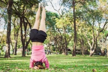 Young woman doing handstand yoga exercise to build her beauty body in the park surround with nature and warm sunshine in the morning. Young woman exercise yoga in the park. Outdoor exercise activity