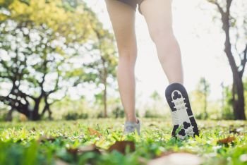 Close up of a young woman’s legs in warming up the body by stretching her legs before morning excercise and yoga on the grass beneath warm light shining. Outdoor excercise concept.