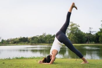 Young asian woman yoga outdoors keep calm and meditates while practicing yoga to explore the inner peace. Yoga have good benefits for health near lake at park. Sport and Healthy lifestyle concept.