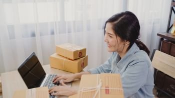Beautiful smart Asian young entrepreneur business woman owner of SME online checking product on stock and save to computer working at home. Small business owner at home office concept.