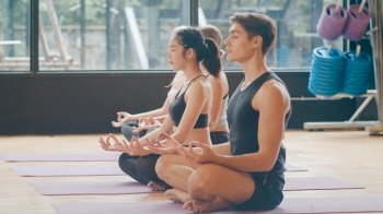 Young diversity sporty people practicing yoga lesson with instructor. Multi racial group of women and man exercising healthy lifestyle in fitness studio. Sport activity, gymnastics or dancing class.