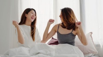 Beautiful young asian women LGBT lesbian happy couple or Girls Friends dancing to streaming music having wild fun in pajamas on bed in teenage bedroom hanging out at home. Spending nice time at home.