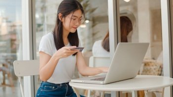 Freelance Asian women online shopping at coffee shop. Young Asia Girl using laptop, credit card buy and purchase e-commerce on internet on table at an outdoor cafe in evening concept.