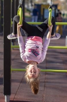 Young girl exercising on gymnastic rings upside down position outside on a playground