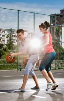 Young man and woman playing basketball on the playground with a light in the background