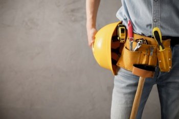 Worker man and tool belt holding construction helmet near wall. Male hand and tools for house room renovation. Home renovation concept