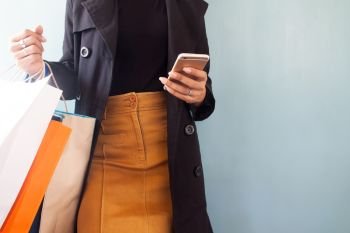 Woman wearing black overcoat using mobile phone and shopping bags on hand, Shopping concept