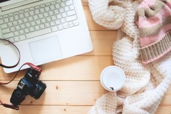 Creative flat lay of traveler’s item, laptop computer, camera, Knitting sweater and takeaway coffee on wooden table, Travel and lifestyle concept