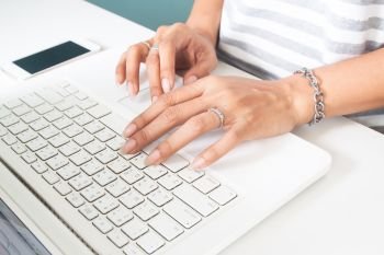 Woman’s hand with wedding ring using laptop computer. Technology and lifestyle concept