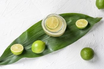 Fresh lemonade in a jar and green limes on a leaf. Above view with a white kitchen table and