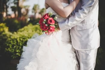 Bride holds a wedding red rose bouquet in hands, the groom hugs . Bride holds a wedding red rose bouquet in hands, the groom hugs his bride together. Wedding lover concept.