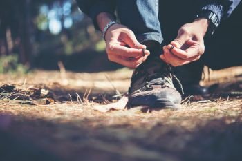 Young hiker man ties the laces on his shoe during a holiday backpacking in forest.. Young hiker man ties the laces on his shoe during a holiday back