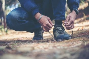 Young hiker man ties the laces on his shoe during a holiday back. Young hiker man ties the laces on his shoe during a holiday backpacking in forest.