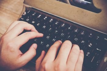 Hands typing on vintage typewriter on wooden table.