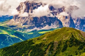 View of the beautiful Dolomites mountain with the clouds floating over the peak and the forest of pine trees, seen at the Secada Peak in South Tyrol, Italy