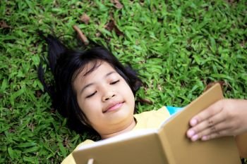 Asian girl are reading a book on lawn in park.