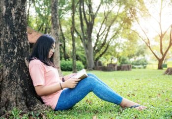 Girl are reading a book on lawn in park with sunlight.