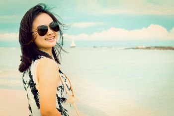 Beautiful woman tourist wearing sunglasse smiling looking at the camera on the beach near the sea at Tarutao island National Park, Satun, Thailand, in green teal and orang color vintage style. Vintage style woman on the beach in Thailand