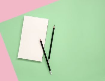 Empty notepad with pencils on green and pink background with copy space.