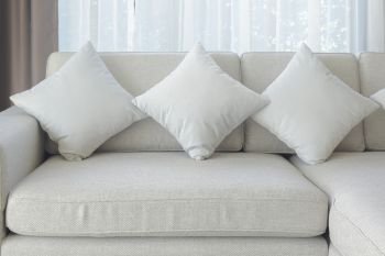 Pillows and sofa in beige color with sheer curtain in background