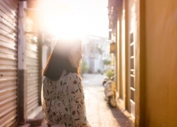 Woman walking on walkway in narrow of village urban landscape at the sunset, looking to the side