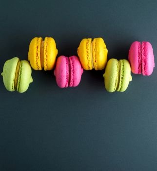 multi-colored round cakes with cream macarons on a black background, copy space