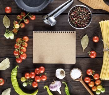 open notepad with brown sheets and ingredients for cooking pasta on a wooden table, view over