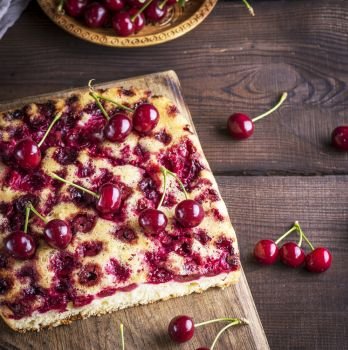 baked cherry pie on a brown wooden board and fresh berries, top view