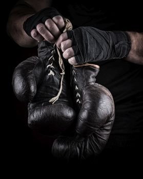  pair of very old boxing sports gloves in men’s hands rewound with a black bandage