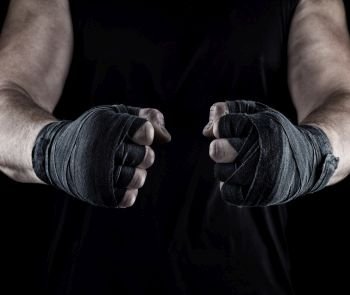  men’s hands wrapped in a black bandage, body parts in front of the torso, black background