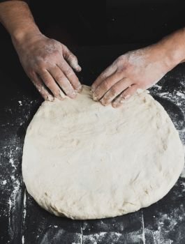 men’s hands knead a round piece of dough for making pizza, top view