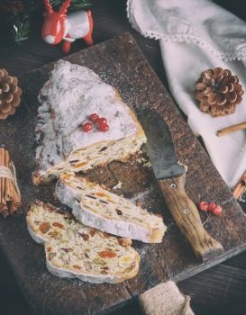 Stollen baked traditional European cake with nuts and candied fruits sprinkled with powdered sugar and cut into pieces on a brown wooden board, top view