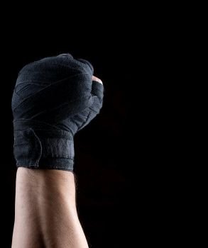 male right hand is wrapped in a black sports textile bandage on a black background, copy space