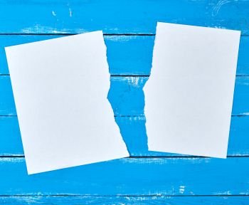 half torn blank white sheet  on a blue wooden background, close up