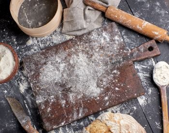 bread, white wheat flour, wooden rolling pin and old cutting board on a black table, top view