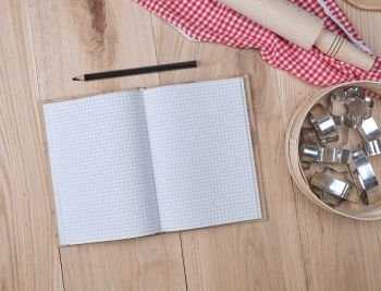 open notebook in a cell, round wooden sieve with baking molds, top view