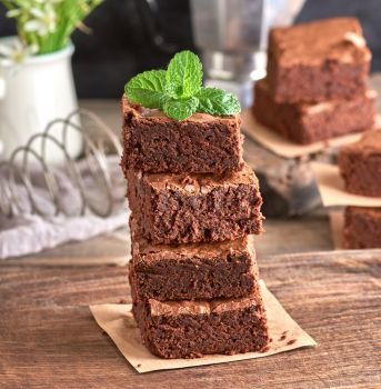 stack of square pieces of baked brownie on a brown wooden board, on top of a cake of mint leaf