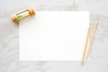 Blank white note paper, hourglass and pencils on white marble background