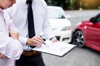 Insurance agent writing on clipboard while examining car after accident claim being assessed and processed