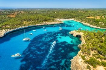 Aerial view of transparent sea with blue water, sandy beach, rocks, green trees, yachts and boats in sunny morning in summer. Travel in Mallorca, Balearic islands, Spain. Top view. Colorful landscape