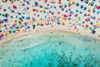 Aerial view of sandy beach with colorful umbrellas, swimming people in sea bay with transparent blue water in sunny morning in summer. Travel in Mallorca, Balearic islands, Spain. Top view. Landscape