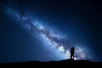 Milky Way. Night landscape with silhouettes of hugging and kissing man and woman on the mountain. Sky with stars. Silhouette of lovers. Couple, relationship. Blue milky way with people. Universe