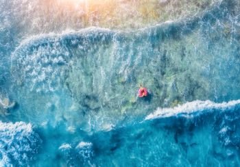 Aerial view of slim young woman swimming on the donut swim ring in the transparent blue sea with waves at sunset. Tropical aerial landscape with girl, clear water, sunlight. Top view. Summer travel