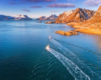 Aerial view of fishing boats, rocks in the blue sea, snowy mountains and colorful sky with clouds at sunset in winter in Lofoten islands, Norway, Landscape with two ship. Top view. Travel. Seascape