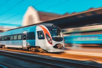 High speed train in motion at the railway station at sunset in Europe. Modern intercity train on the railway platform with motion blur effect. Industrial scene. Passenger transportation on railroad