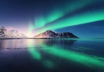 Northern lights in Lofoten islands, Norway. Green Aurora borealis. Starry sky with polar lights. Night winter landscape with aurora, sea with sky reflection, rocks, beach and snowy mountains. Nature