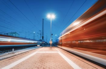 Two high speed trains in motion on the railway station at night. Moving blurred modern intercity train on the railway platform in Europe. Passenger railway transportation. Railroad at twilight. Travel