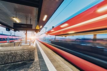 High speed train in motion on the railway station at sunset. Moving blurred modern intercity train on the railway platform in Europe. Passenger railway transportation. Railroad at twilight. Travel